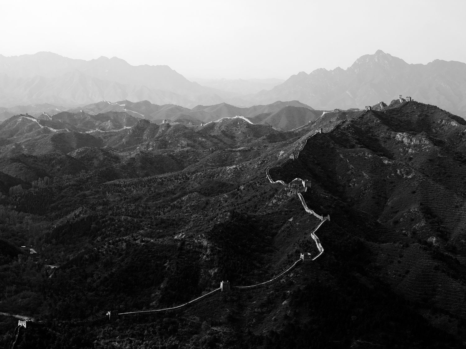 Black and white aerial view of the Great Wall of China winding through misty mountain ranges.