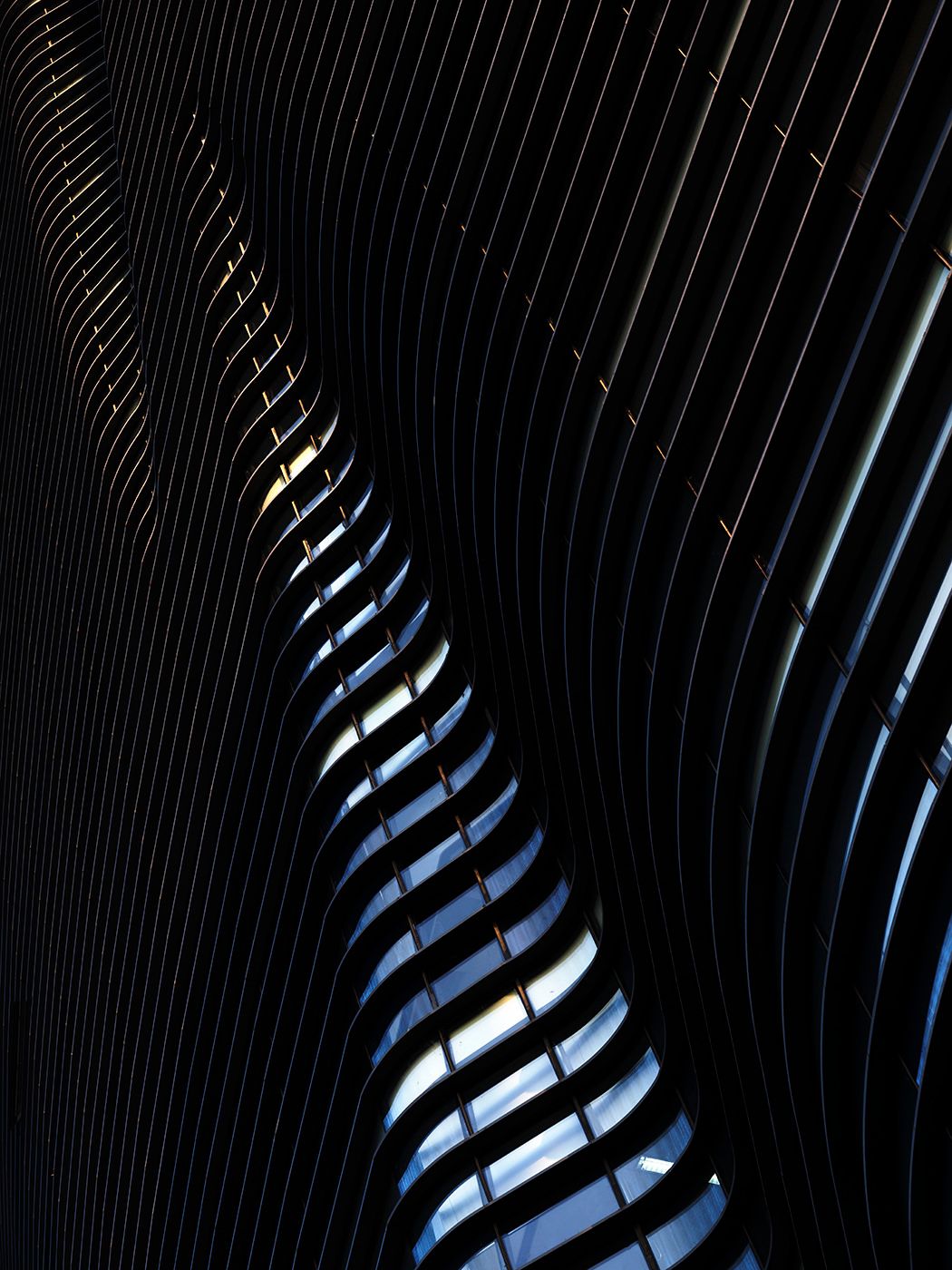 Abstract architectural detail showing curved dark metal fins with dramatic light and shadow contrast.