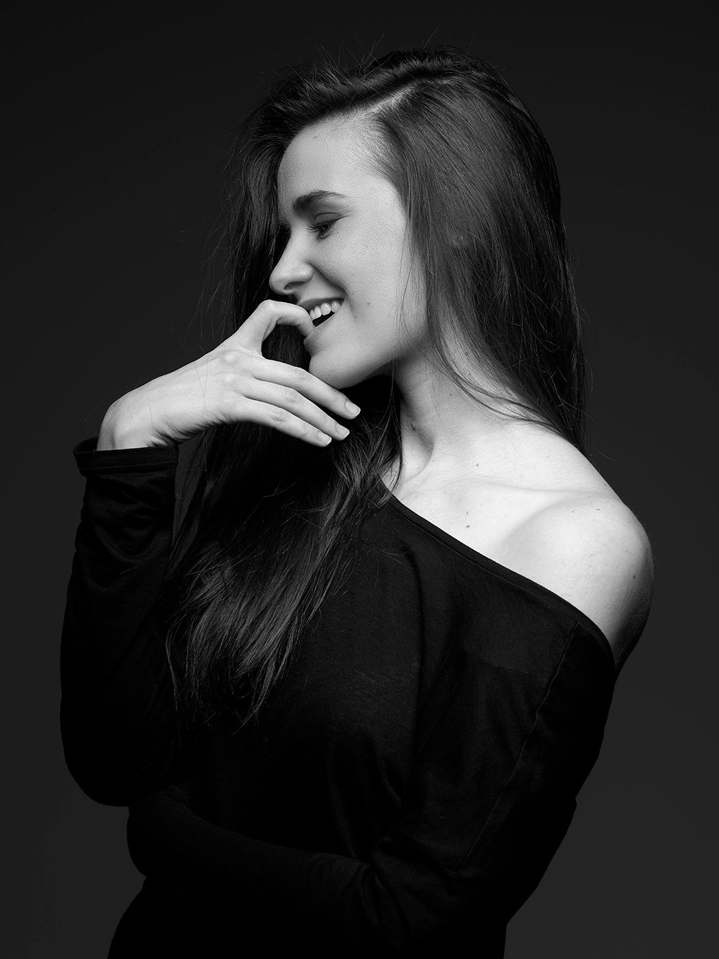 Black and white photo of a young woman in an off-shoulder top laughing with hand near face.