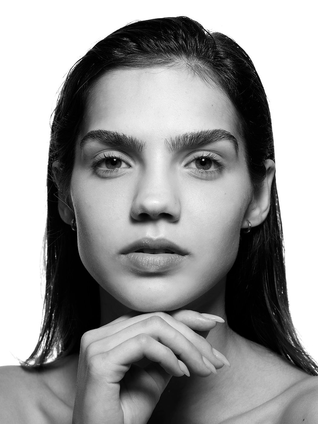 Black and white portrait of a young woman with slicked-back hair, hands clasped under her chin, looking directly at camera.