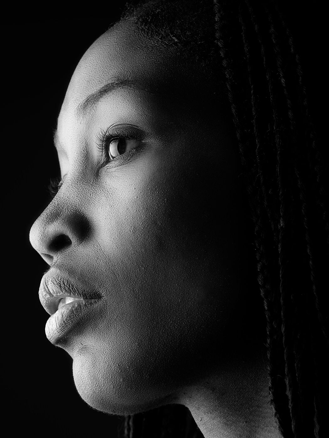 Black and white profile portrait of a young Black woman with braids, dramatic side lighting highlighting her features.