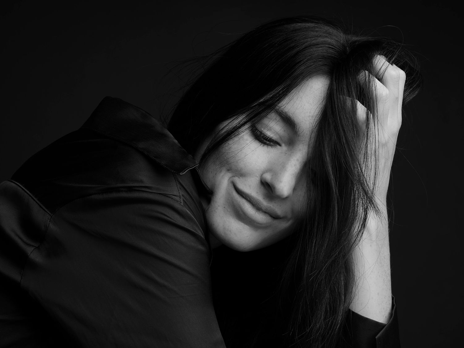 Black and white portrait of a smiling woman with long hair, eyes closed, resting her head on her hand.