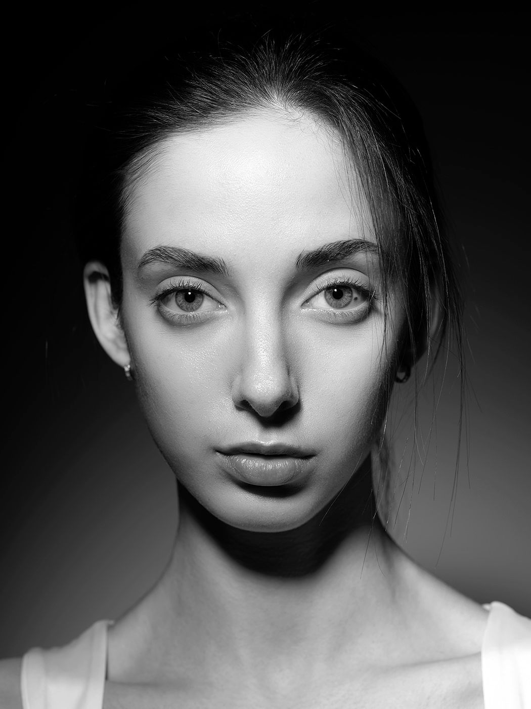 Black and white portrait of a young woman with hair pulled back, wearing a white top, gazing directly at camera.