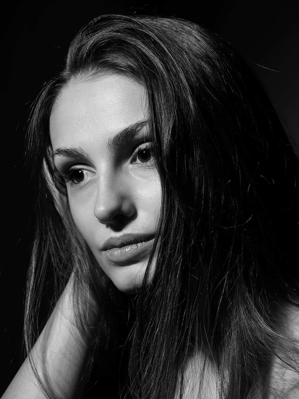Black and white portrait of a young woman with long dark hair, gazing softly at the camera against a dark background.