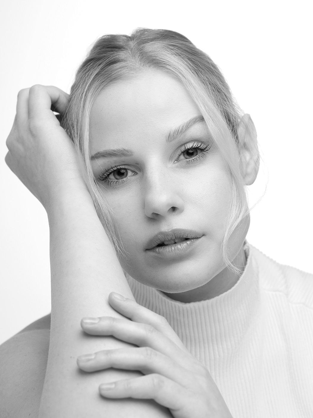 Black and white portrait of a young blonde woman in a white turtleneck, posing gracefully with hand near face.