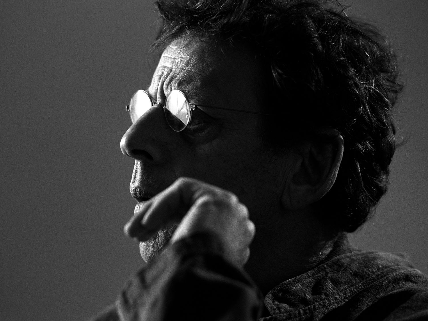 Black and white side profile of a man wearing round glasses with hand raised to chin. Philip Glass, composer