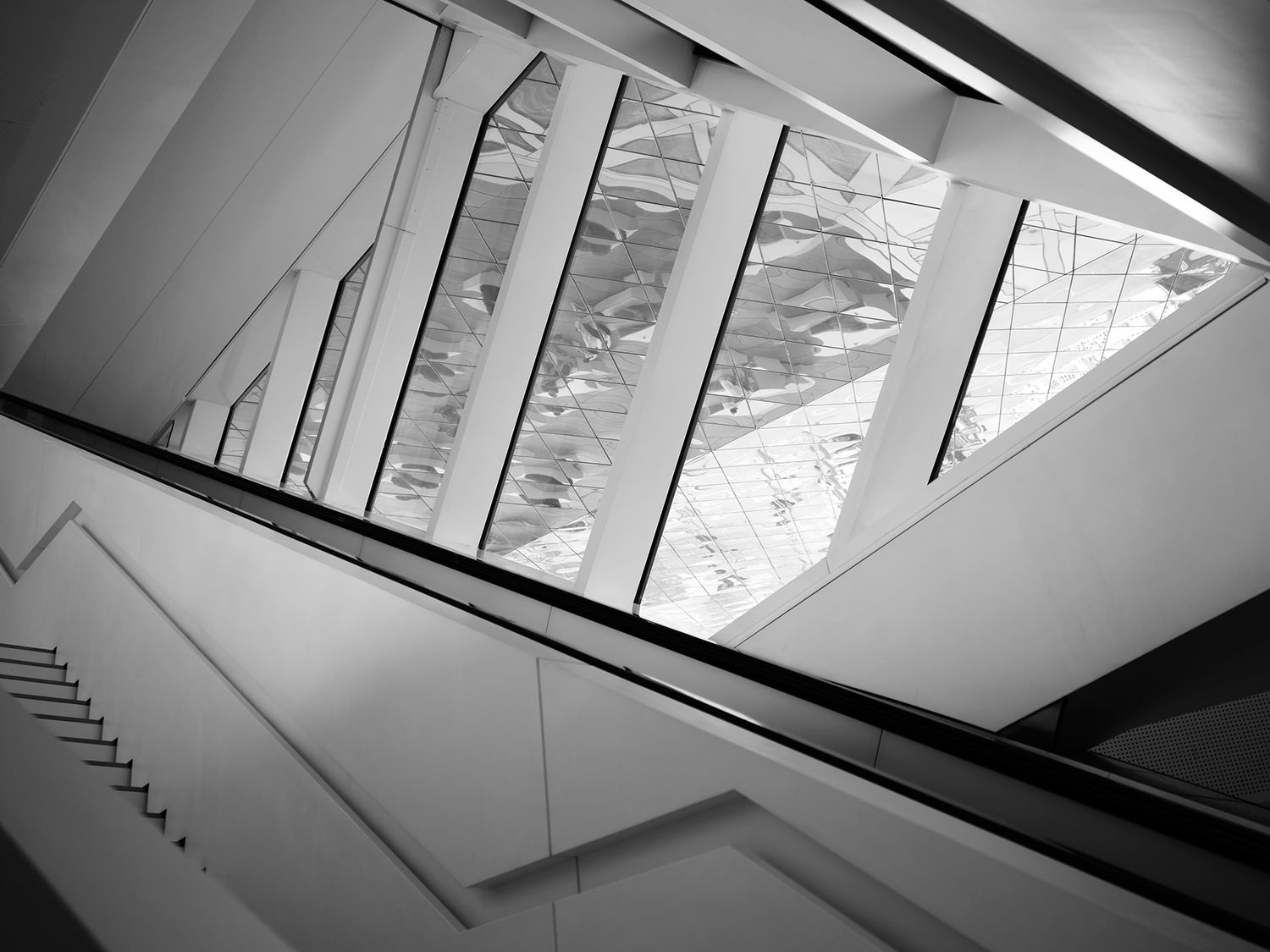 Black and white interior architectural photo showing geometric staircase angles and large angular skylights.