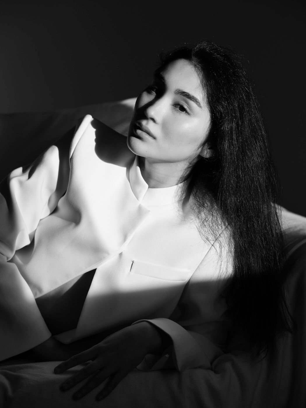 Black and white artistic portrait of a woman with long dark hair wearing a white oversized top.