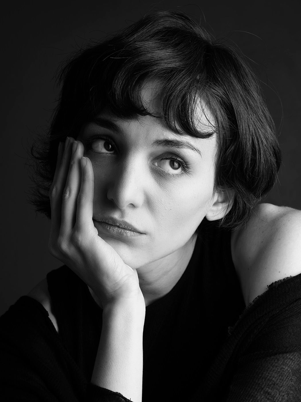 Black and white portrait of a young woman with short dark hair resting her chin on her hand, looking upward thoughtfully.