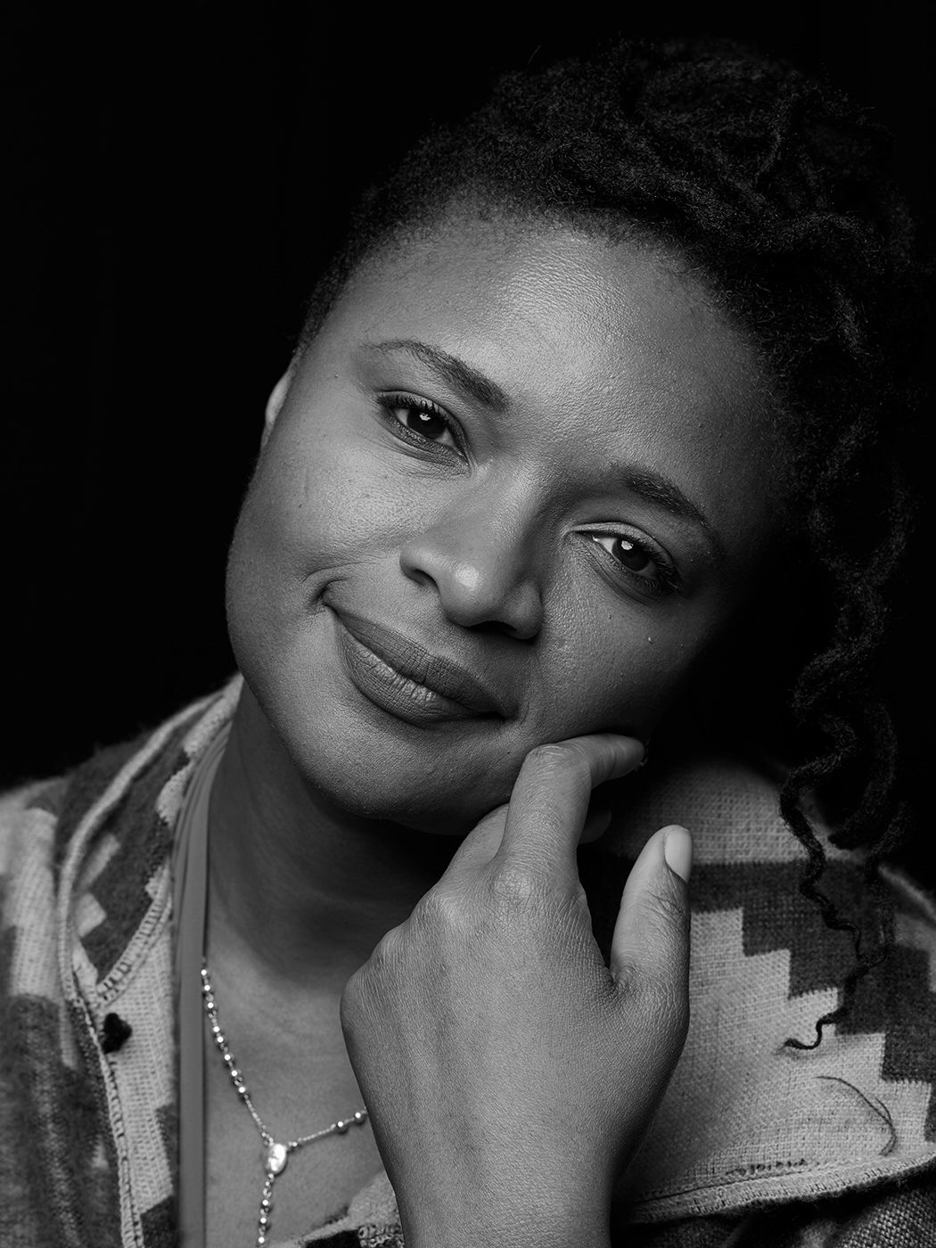 Black and white portrait of a young woman smiling gently with her hand resting on her chin. Lizz Wright