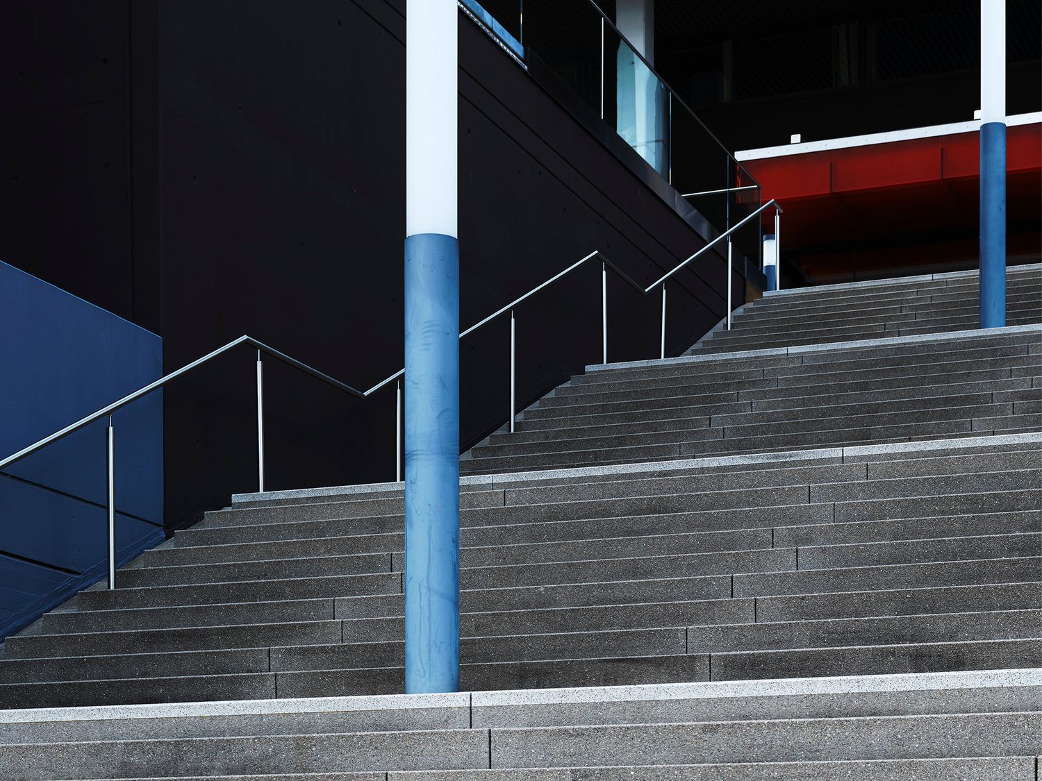 Modern concrete stairs with blue pillars, metal railings, and colorful building facade in an urban architectural setting.