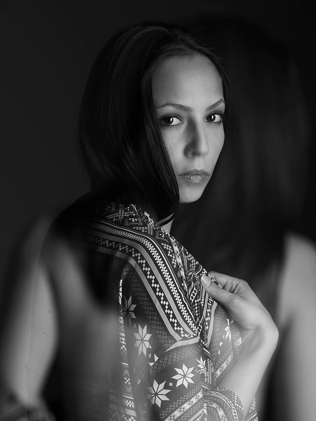 Black and white portrait of a young woman with dark bob hair wearing a patterned dress, looking over her shoulder.