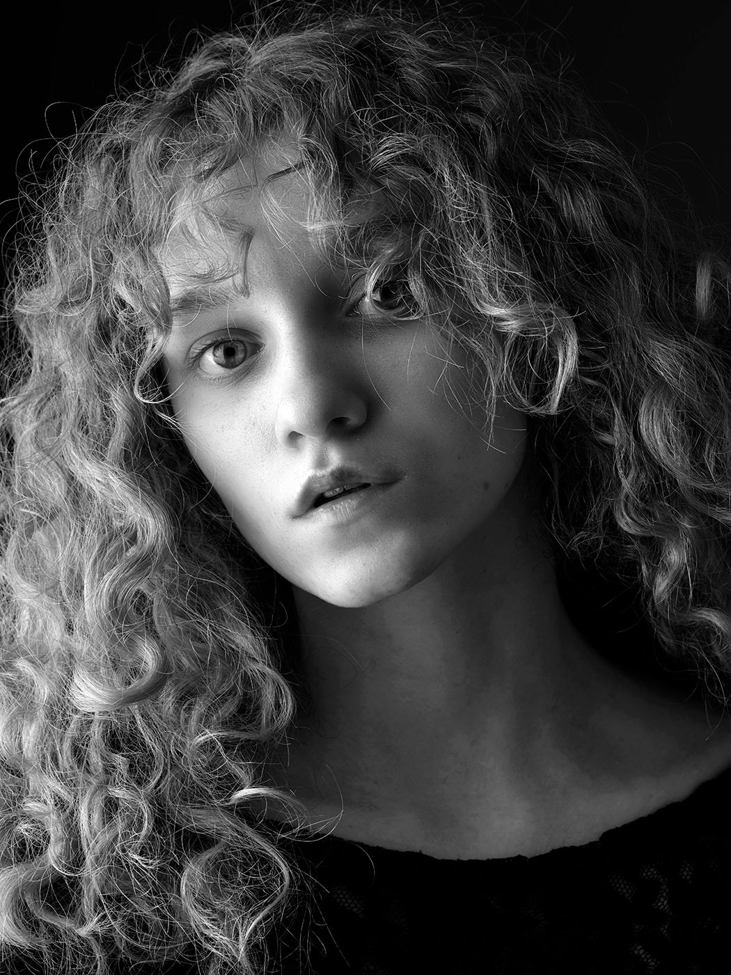 Black and white portrait of a young woman with voluminous curly hair, gazing softly at the camera.
