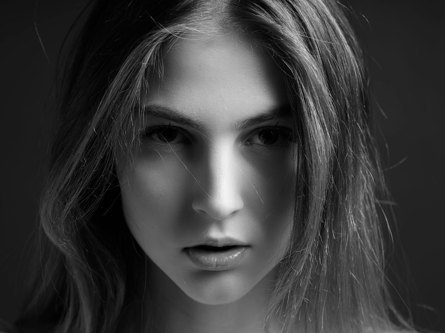 Black and white portrait of a young woman with long hair and intense gaze, studio photography.