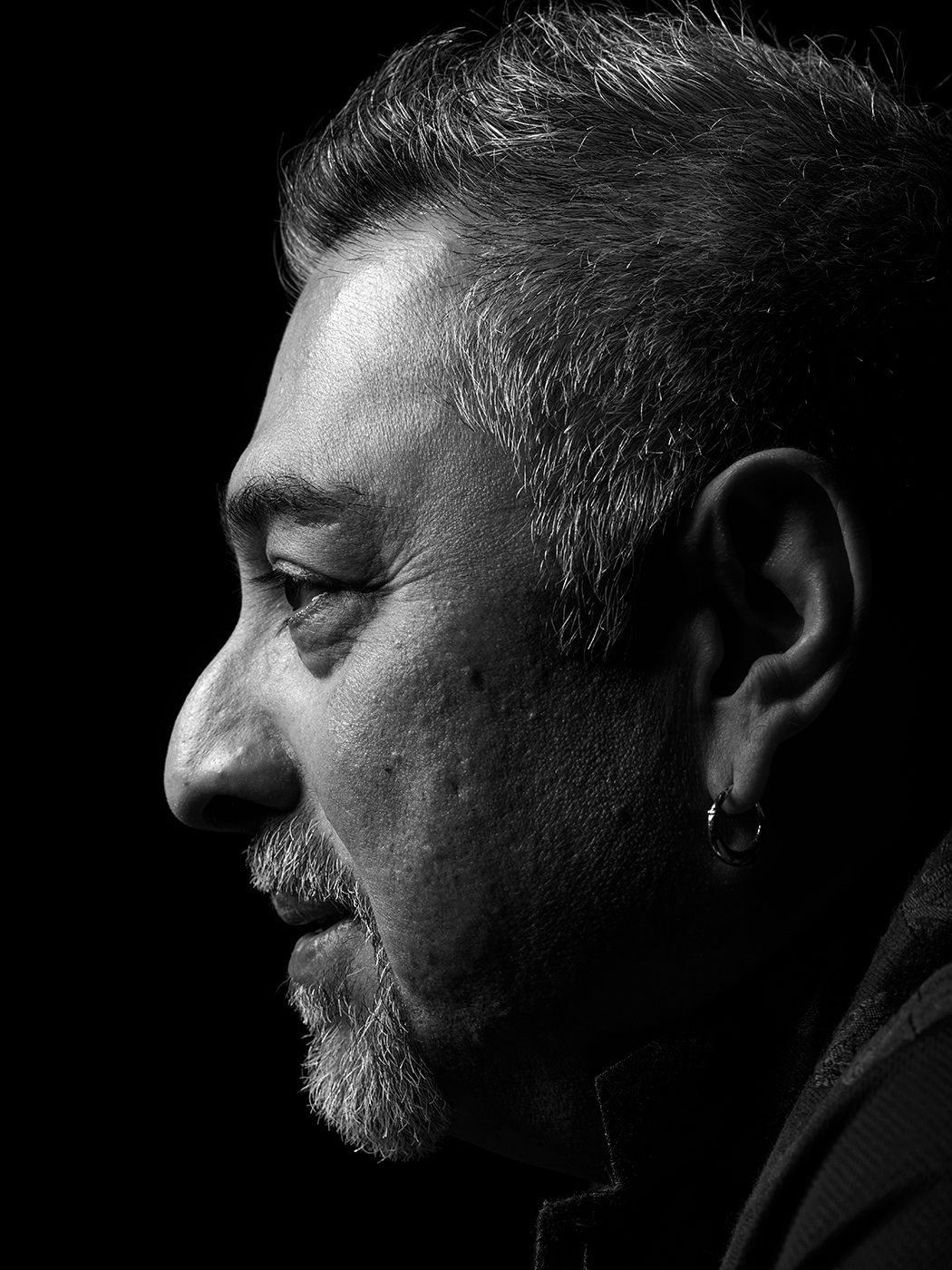 Black and white side profile portrait of a middle-aged man with gray hair, beard, and an earring. Ranjit Barot, musician, drummer.
