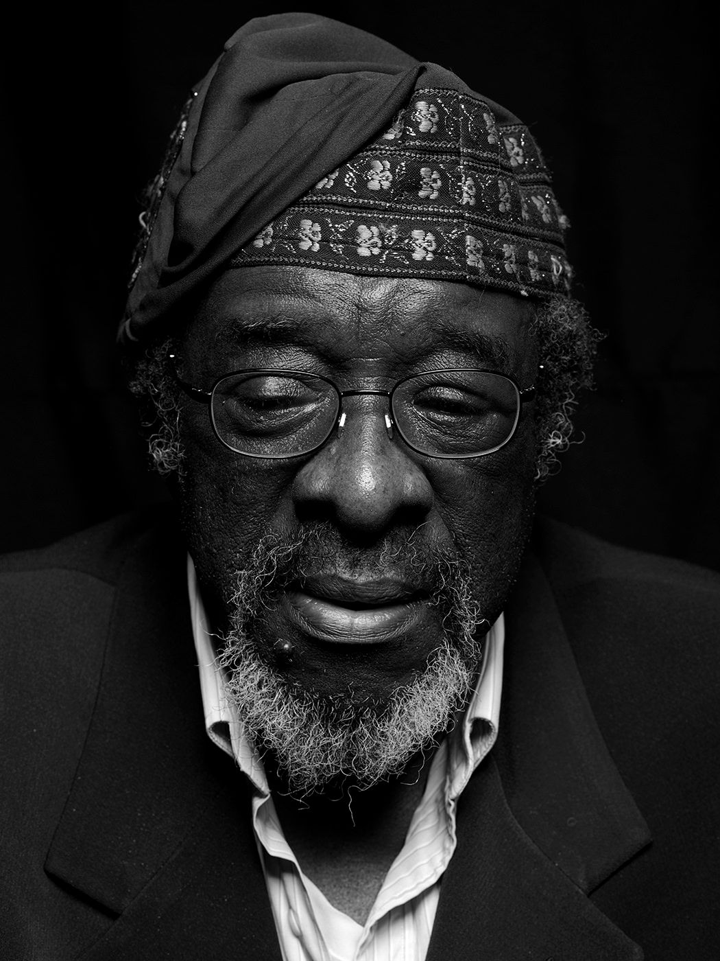 Black and white portrait of an elderly man wearing a decorative kufi cap and glasses, with a goatee beard. James Blood Ulmer