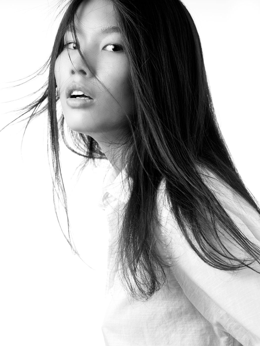 Black and white portrait of a young woman with long dark hair blowing in the wind, looking over her shoulder.