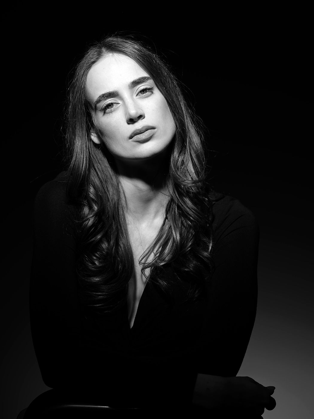 Black and white portrait of a young woman with long hair wearing a black top, dramatic studio lighting.