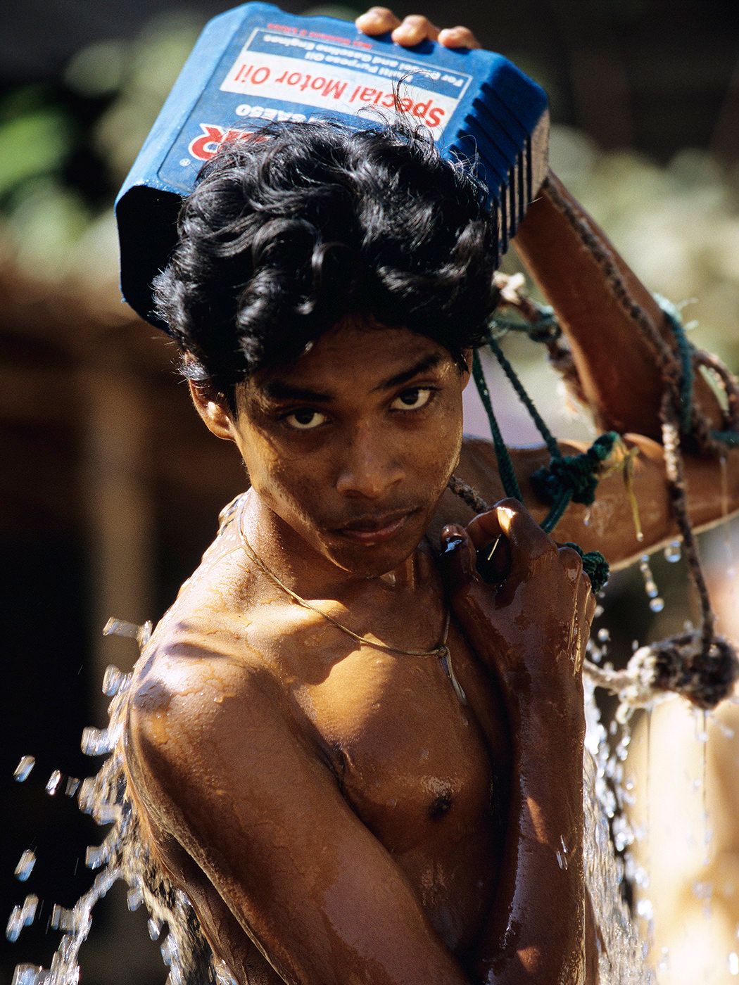 Young man pouring water over his head from a Special Motor Oil container outdoors.