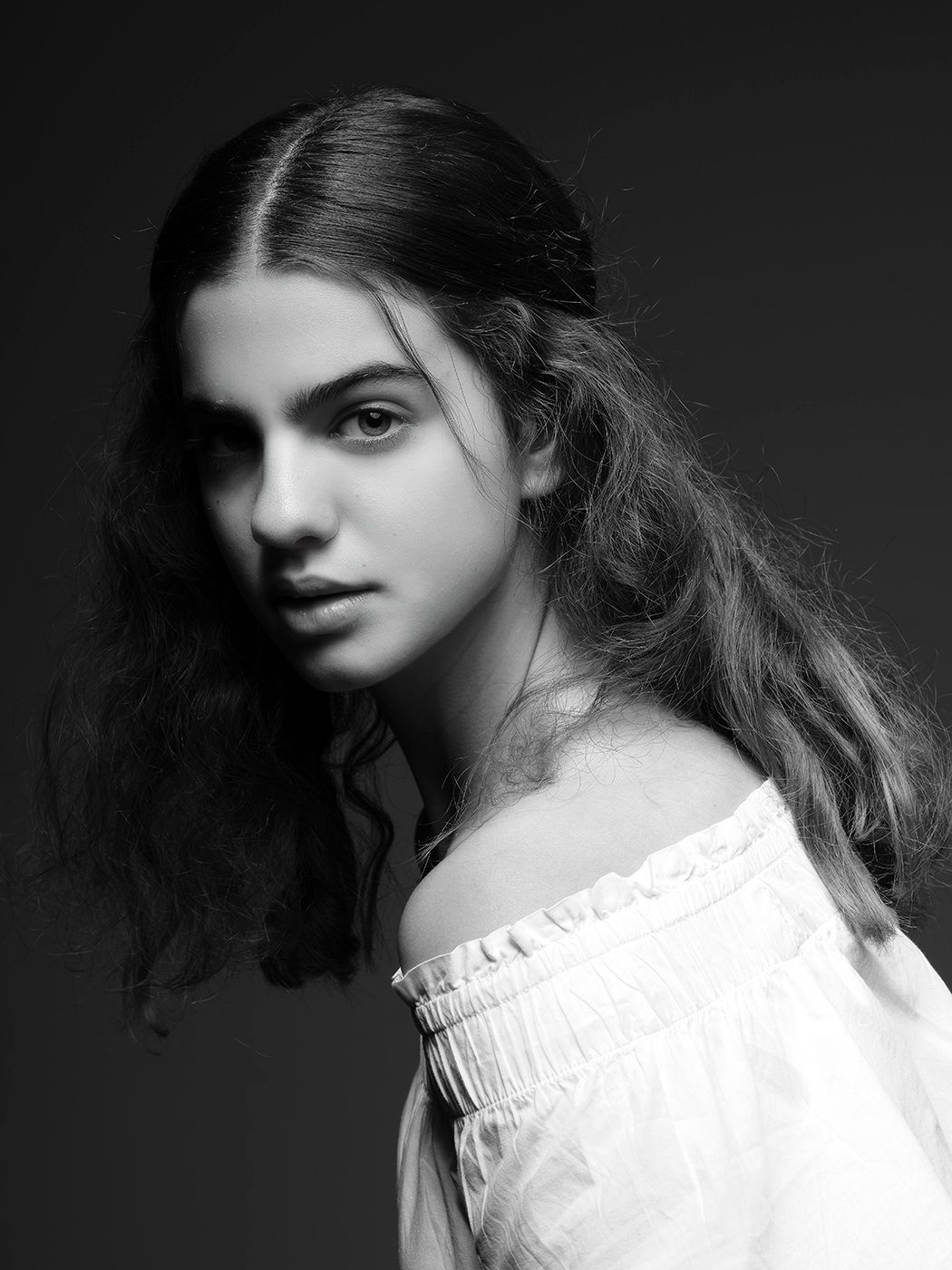 Black and white portrait of a young woman with long hair wearing an off-shoulder white ruffled top.