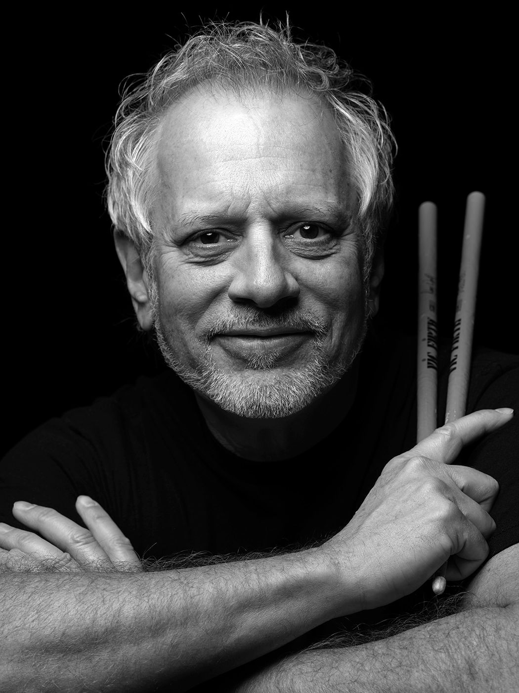 Black and white portrait of a middle-aged man with gray hair holding drumsticks, smiling confidently at the camera. Dave Weckl