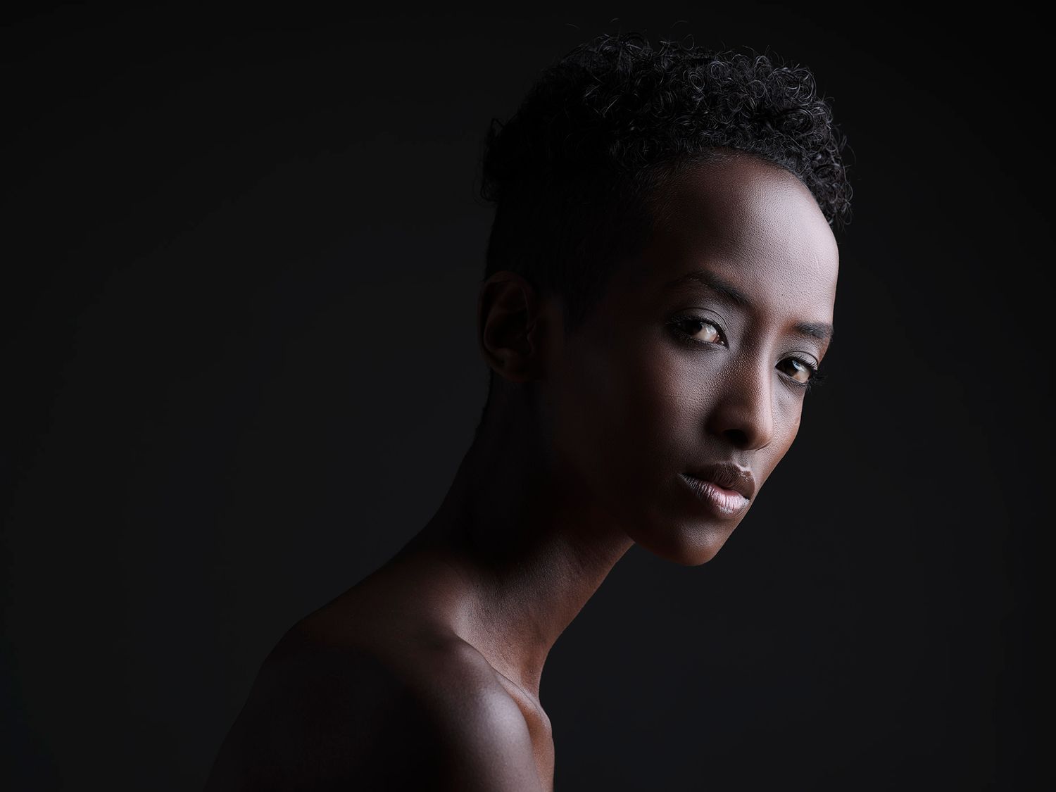 A young Black woman with short natural hair poses against a dark background in a striking studio portrait.