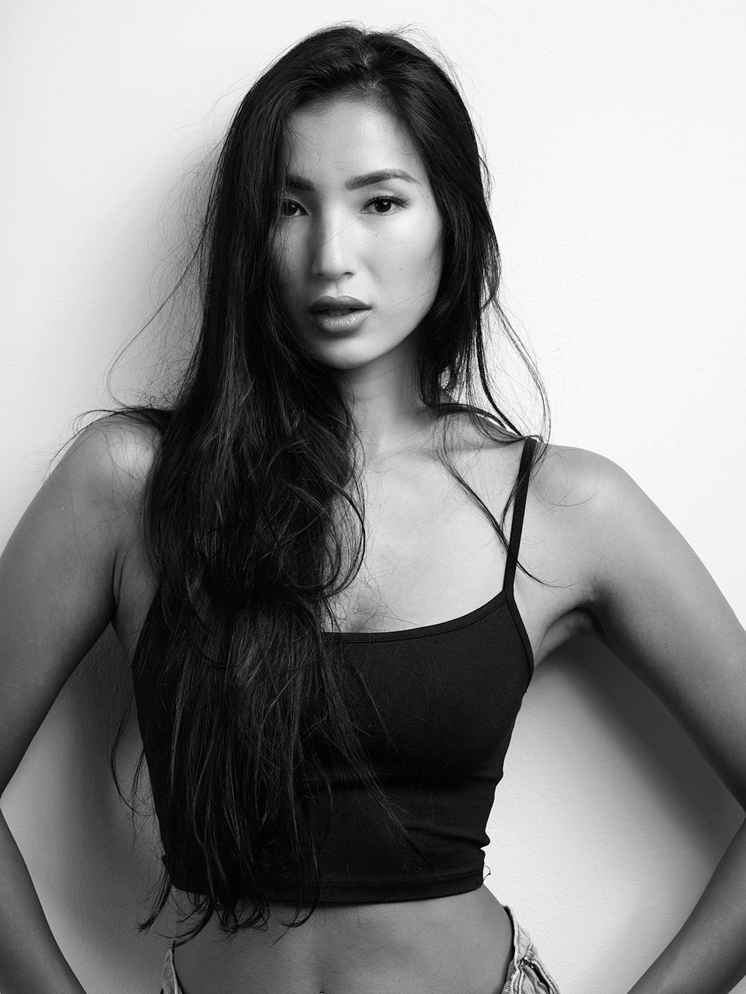 Black and white portrait of a young woman with long dark hair wearing a black crop top, hands on hips.