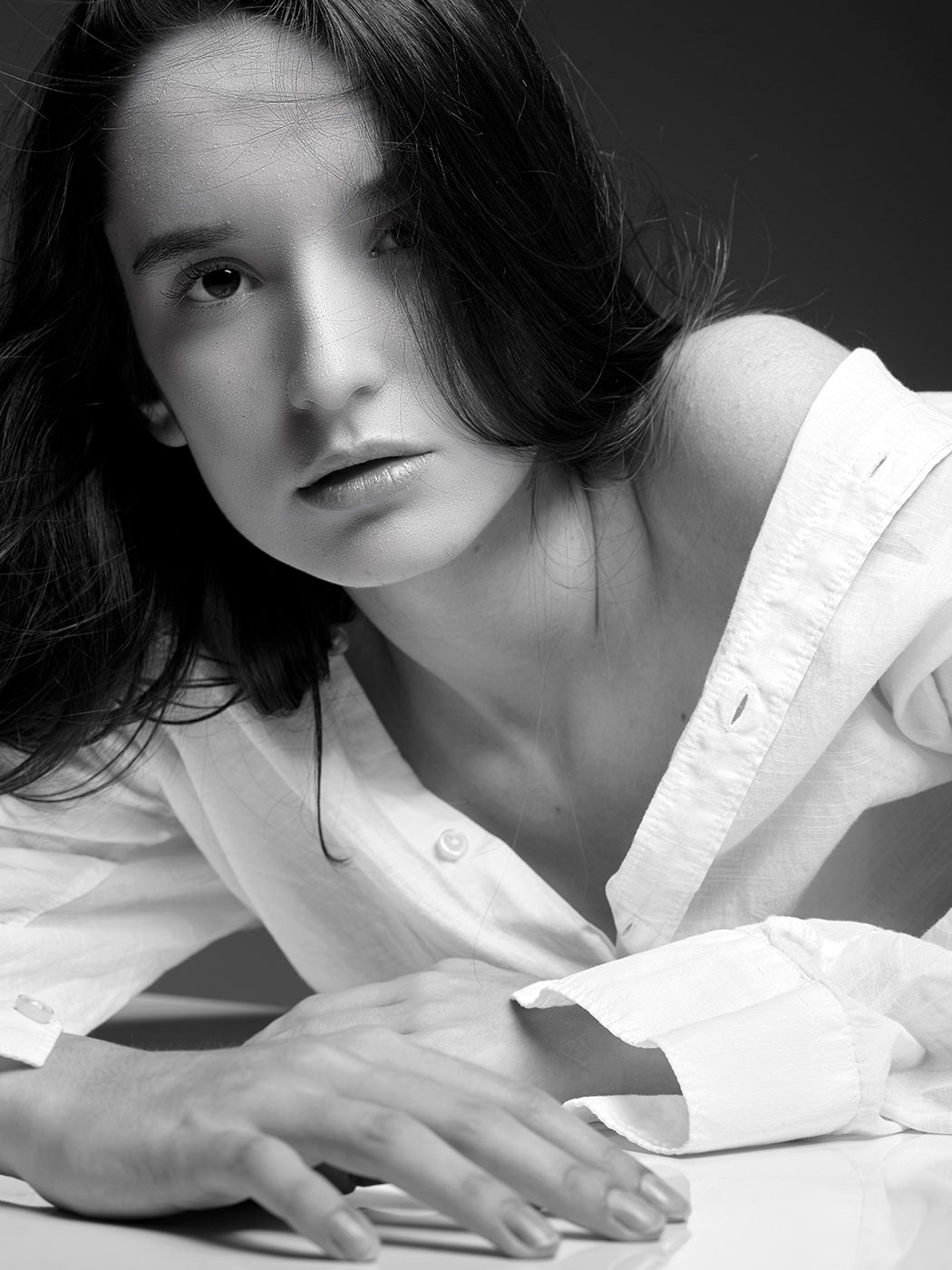 Black and white portrait of a young woman in a white shirt, leaning forward with a serious expression.