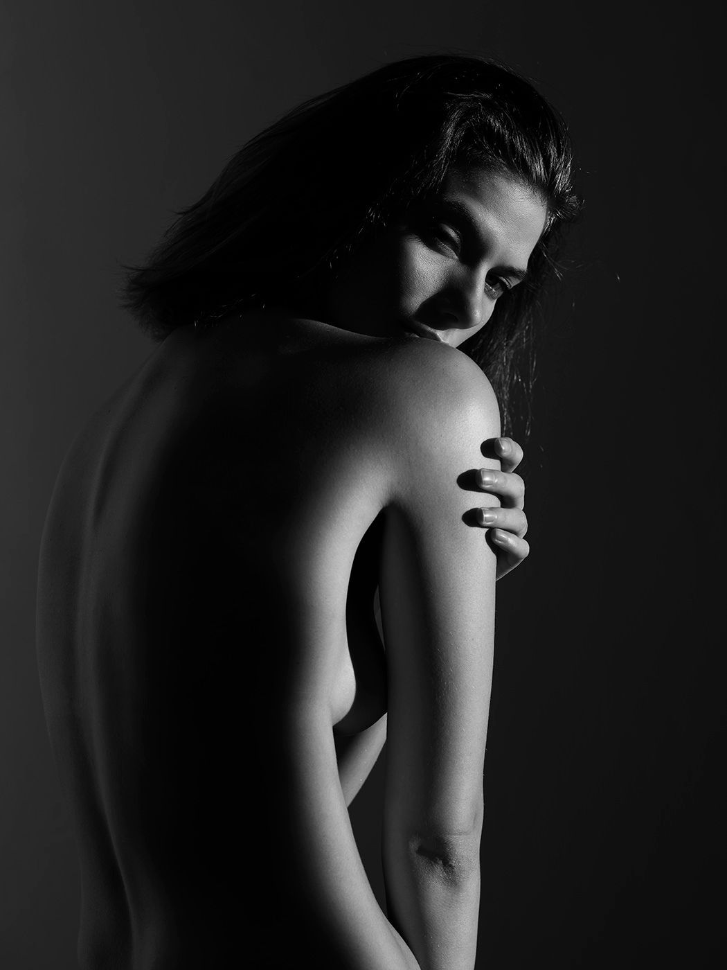 Black and white artistic photo of a woman hugging her shoulders, hair flowing softly.