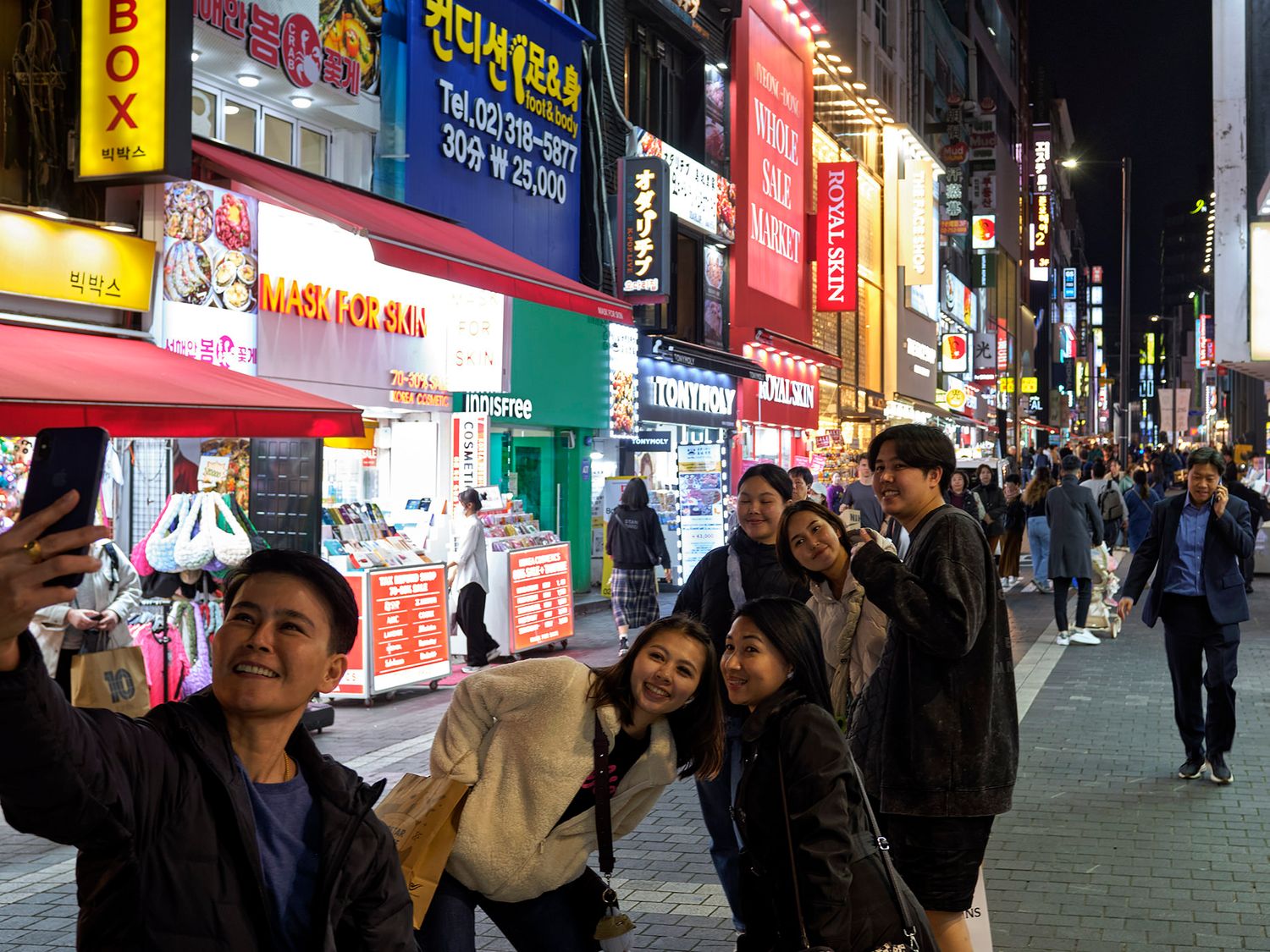Group of friends taking a selfie on a busy neon-lit street in Seoul, South Korea at night.