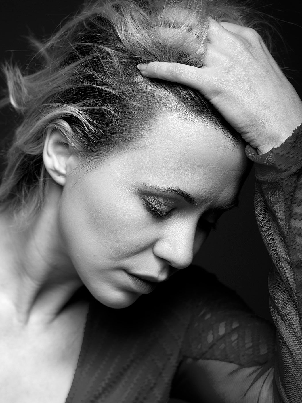 Black and white portrait of a woman with eyes closed, hand resting in her tousled hair, in a contemplative pose.