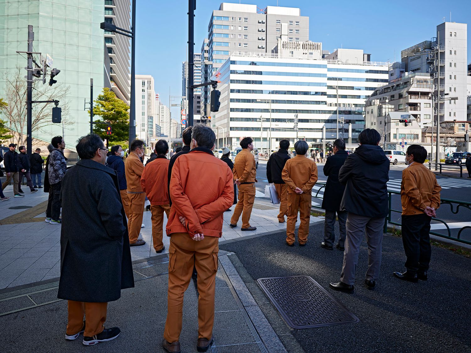 Group of workers in orange uniforms standing on a city street with modern buildings in the background.
