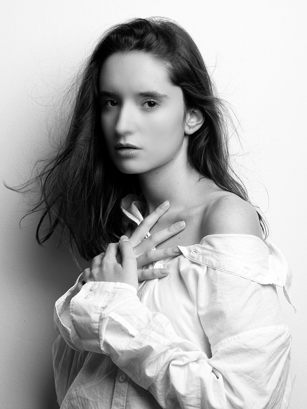 Black and white portrait of a young woman with long dark hair wearing an off-shoulder white blouse, posing elegantly.