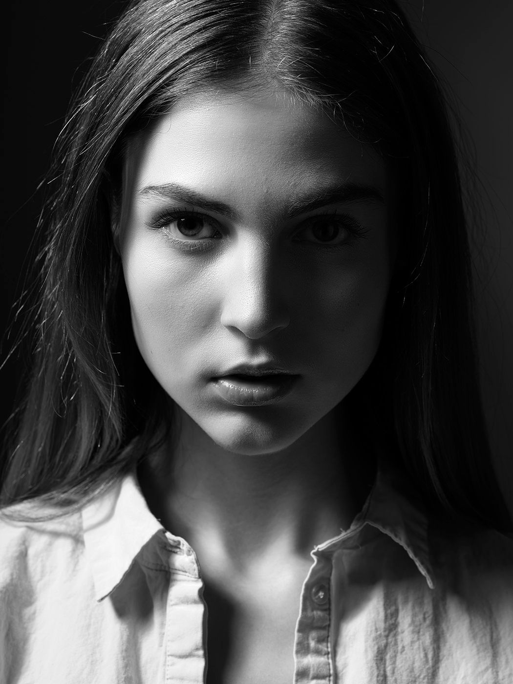 Dramatic black and white close-up portrait of a young woman in a white shirt with intense gaze.
