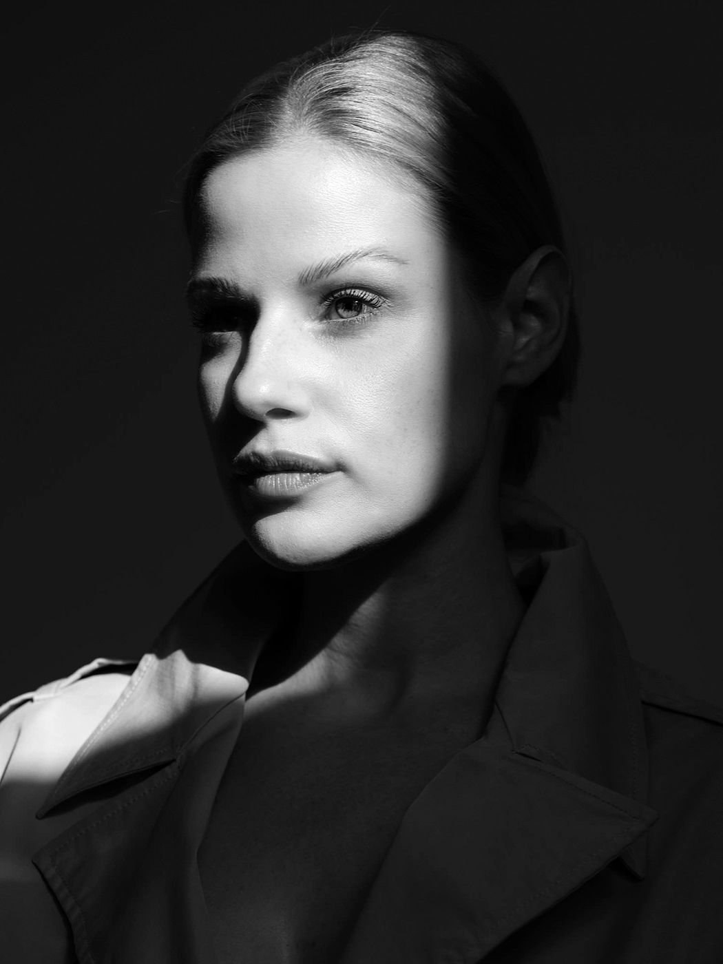 Black and white portrait of a woman in a trench coat with dramatic lighting and sleek hair.