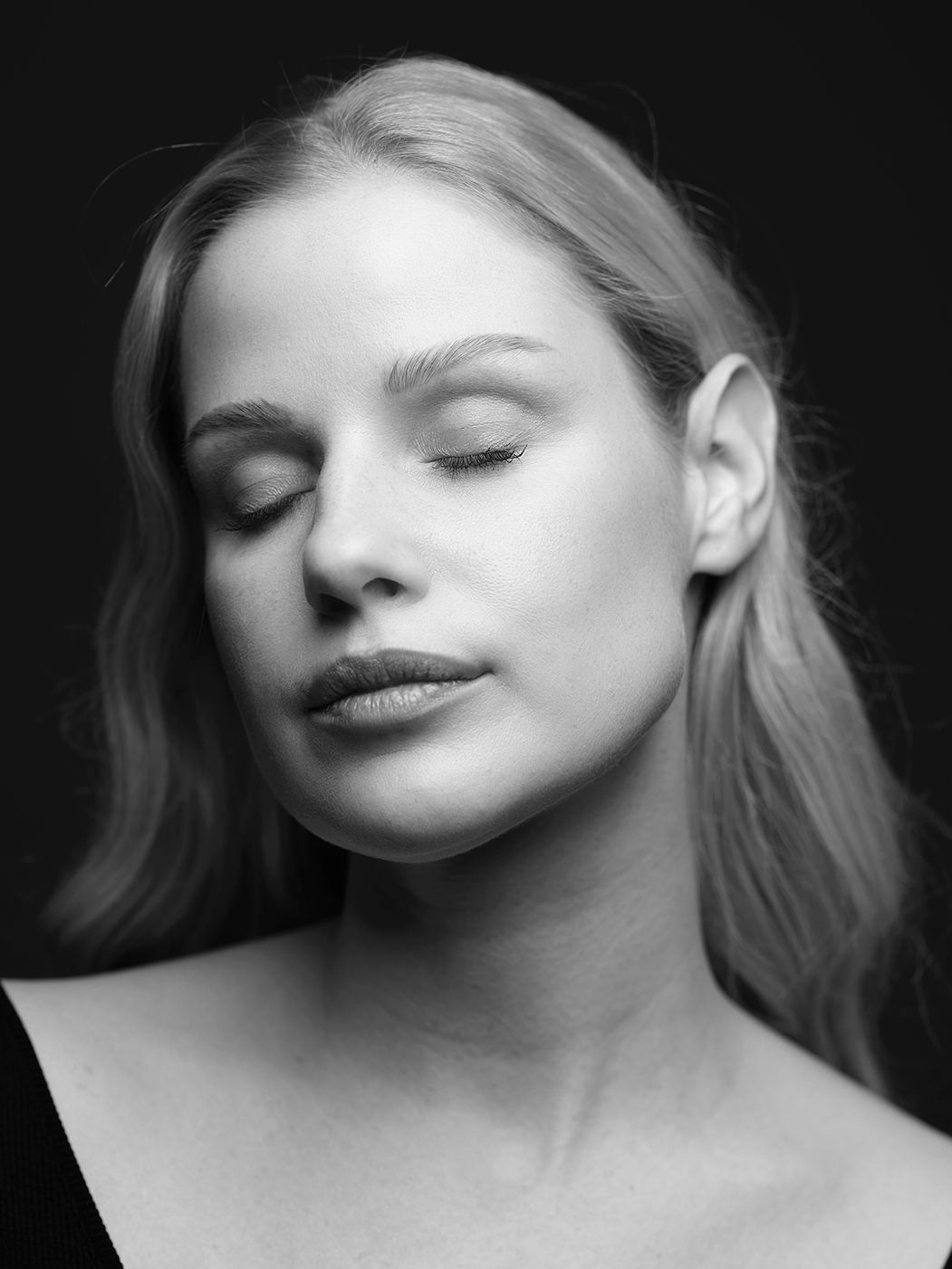 Black and white portrait of a young woman with closed eyes and long blonde hair against a dark background.