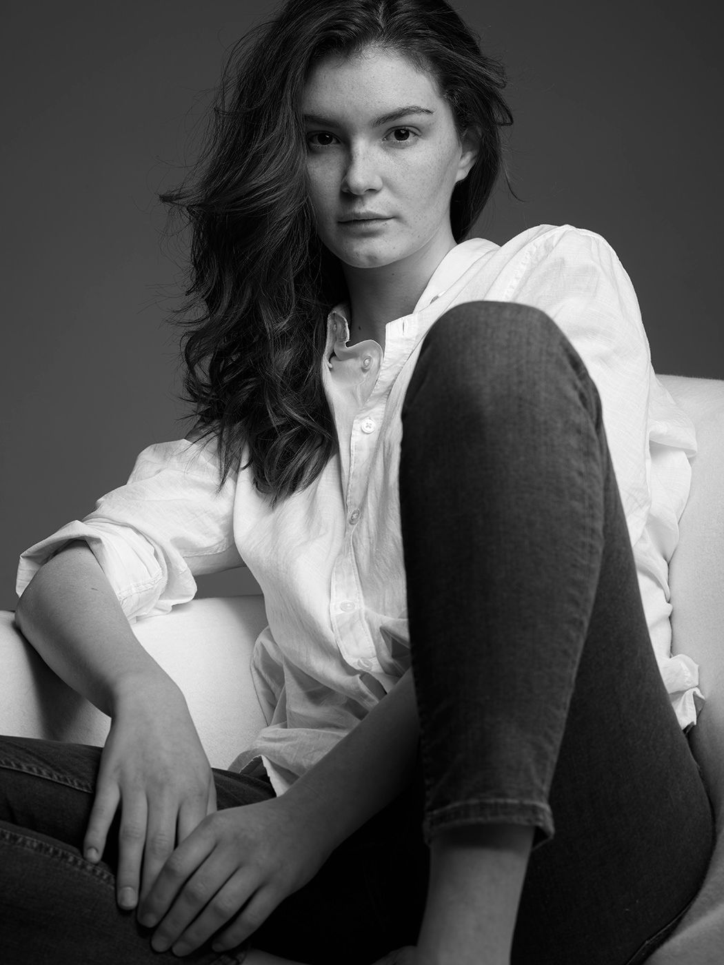Black and white portrait of a young woman in white shirt and jeans seated in a chair.