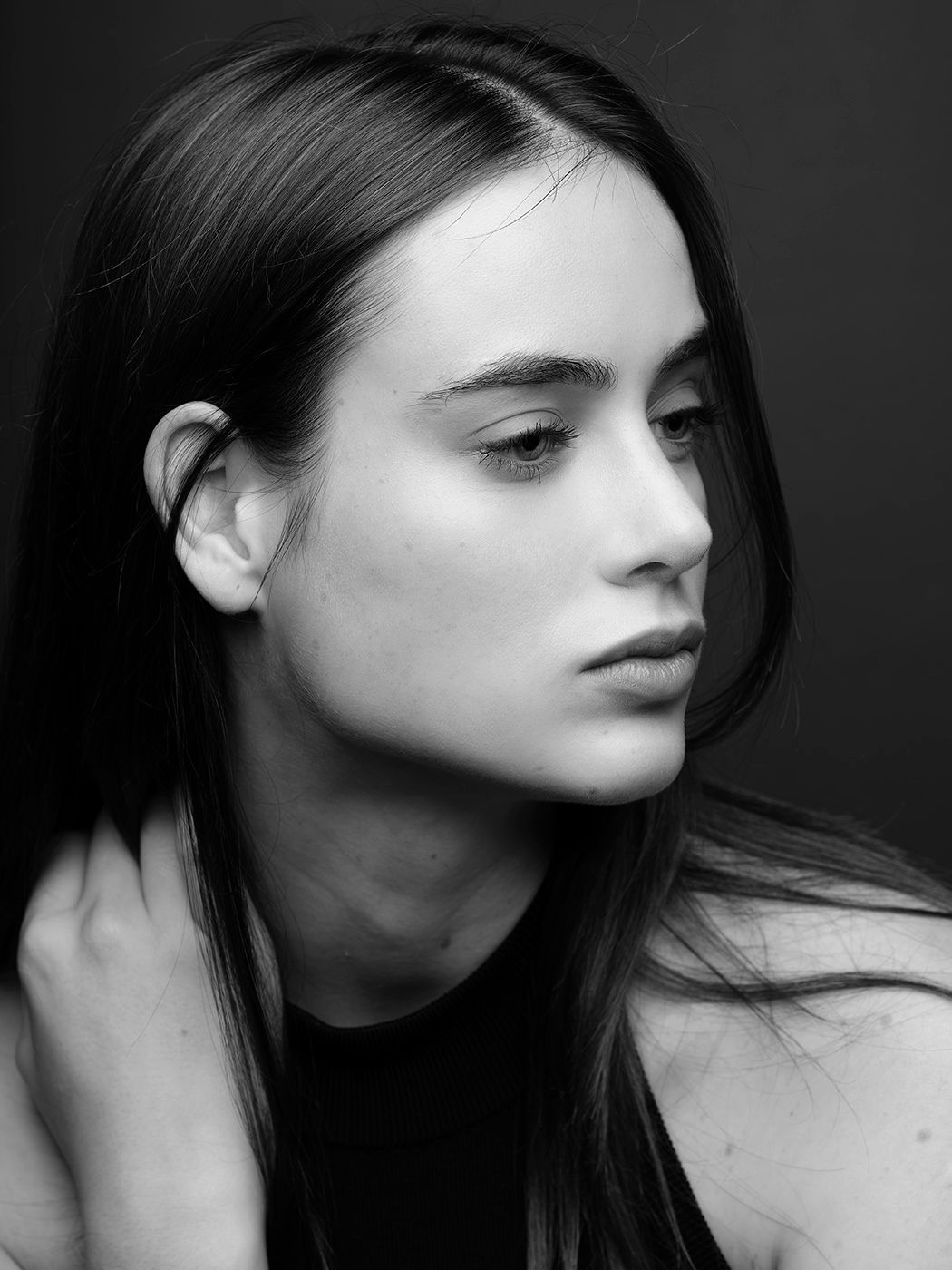 Black and white portrait of a young woman with long dark hair, looking sideways in a studio setting.