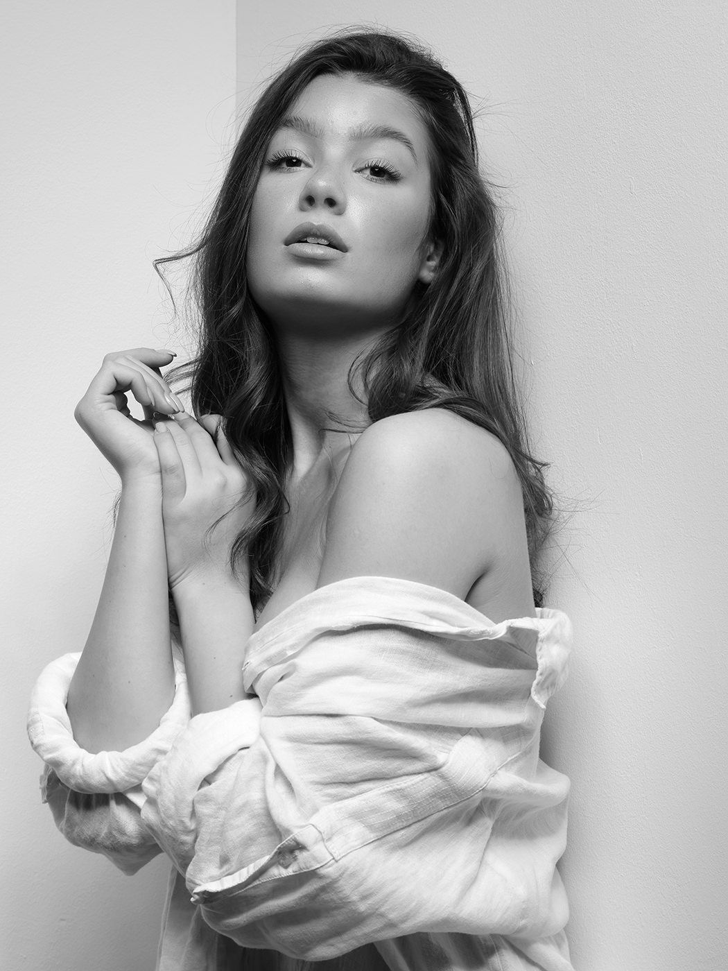 Black and white portrait of a young woman in an off-shoulder white blouse, posing gracefully against a light background.