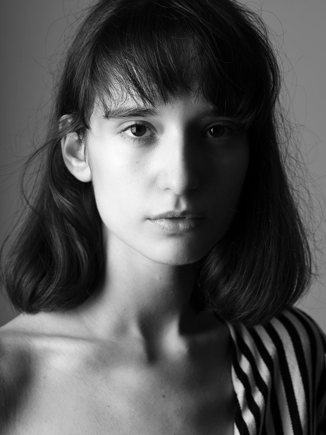 Black and white portrait of a young woman with bangs and shoulder-length hair wearing a striped top.