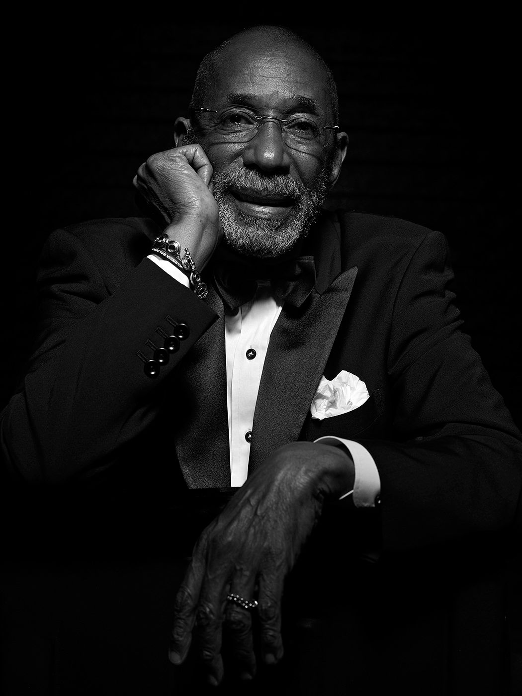 Elegant older man in tuxedo with bow tie poses confidently in dramatic black and white portrait photography. Ron Carter, musician, bass.