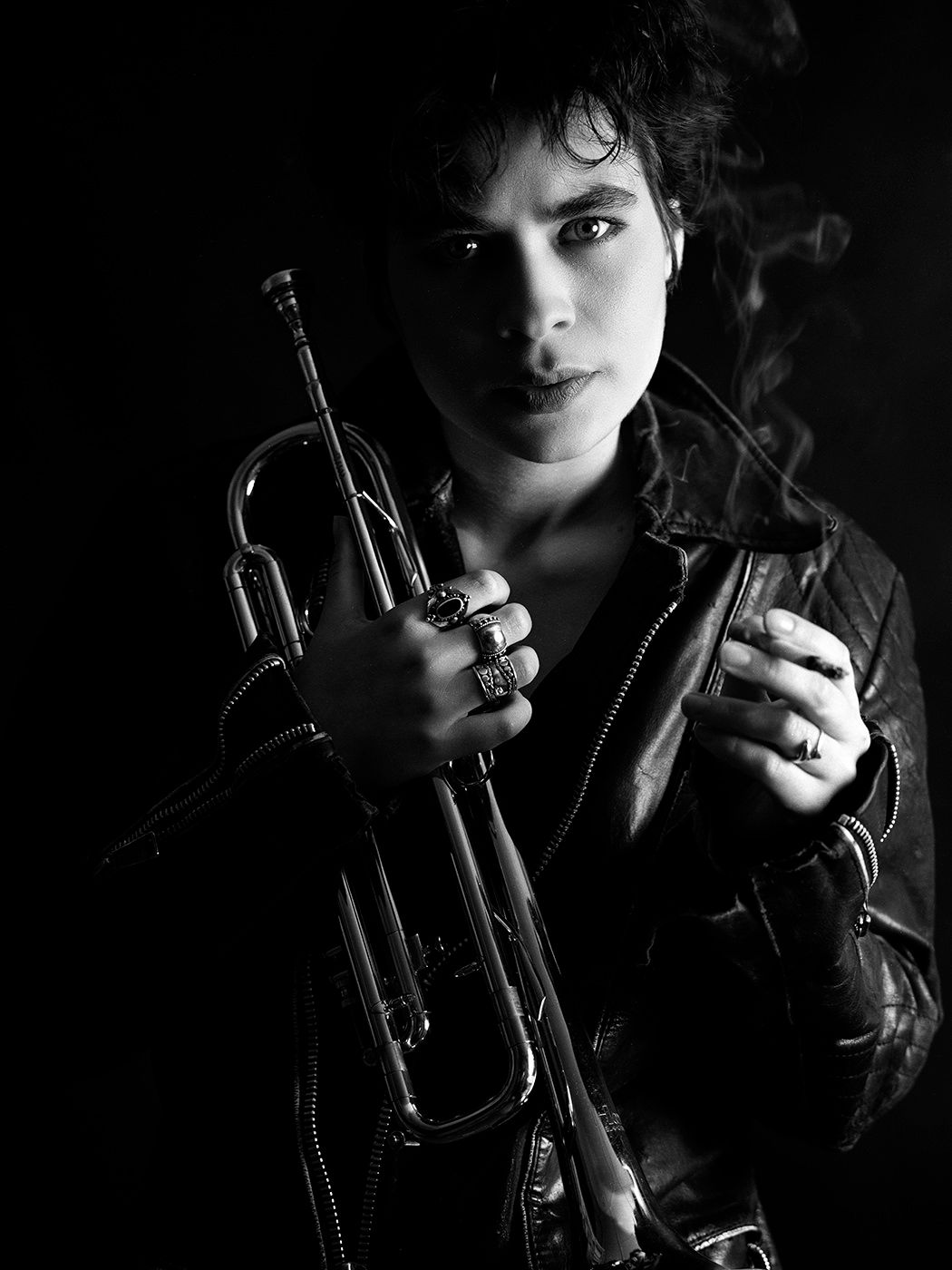 Black and white portrait of a musician holding a trumpet, wearing rings and a leather jacket, with dramatic lighting. Balogh Mari