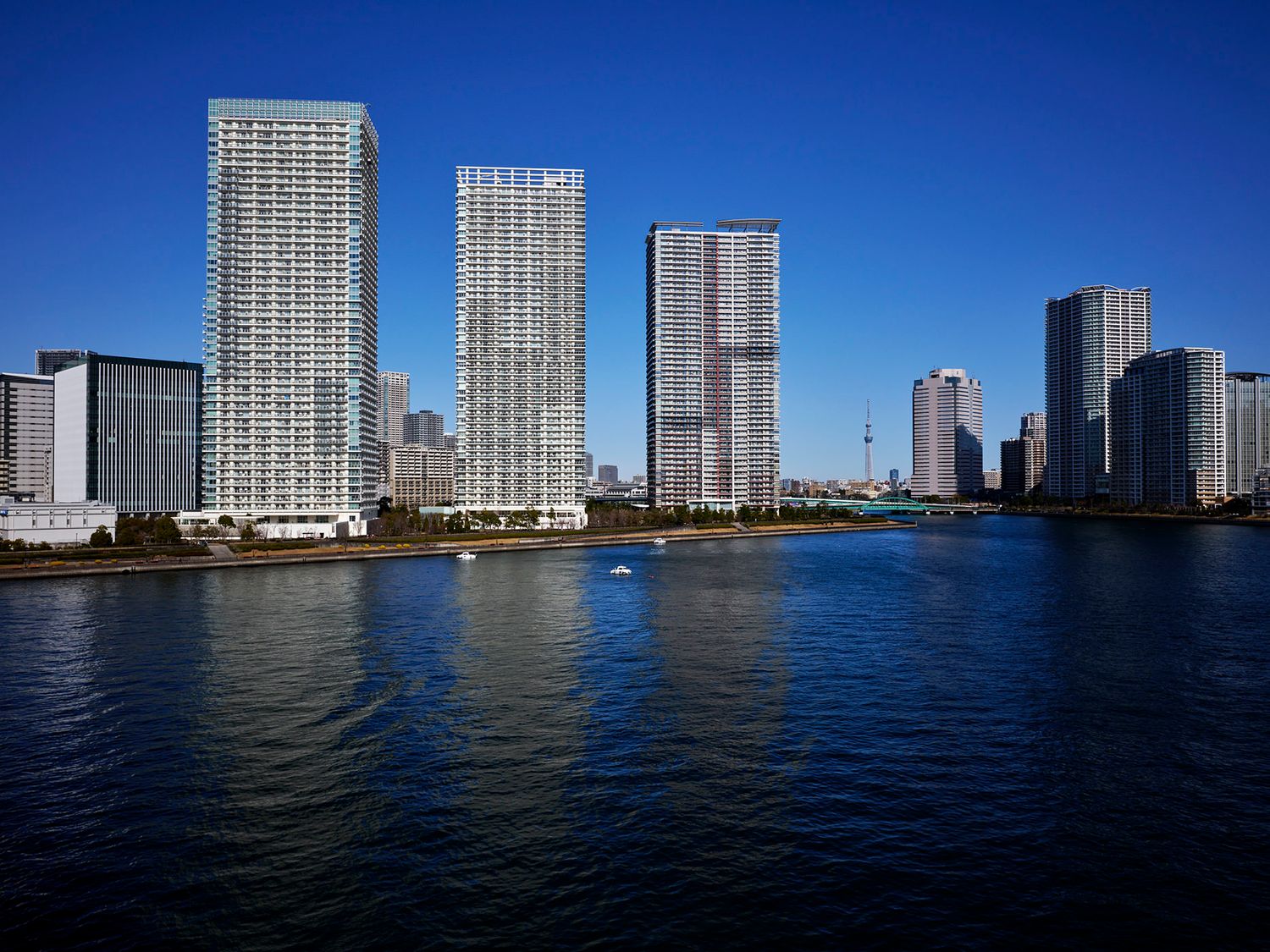 Stunning Tokyo skyline with modern skyscrapers reflecting on calm blue river waters under a clear sky.