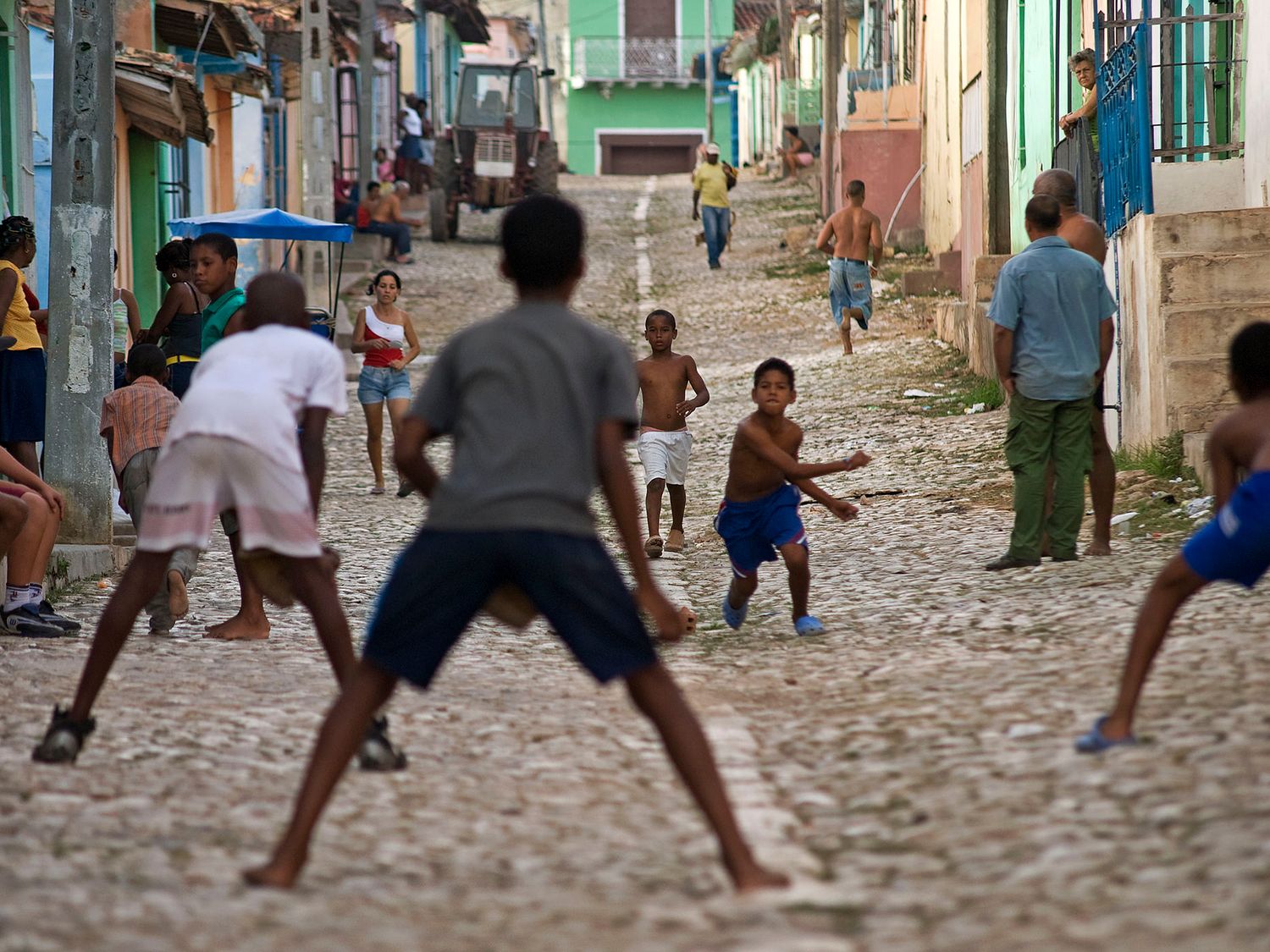 Children playing street soccer on a cobblestone road in a colorful Cuban neighborhood.