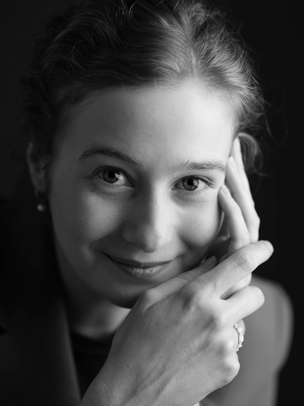 Black and white portrait of a smiling young woman resting her face on her hand with a ring visible.