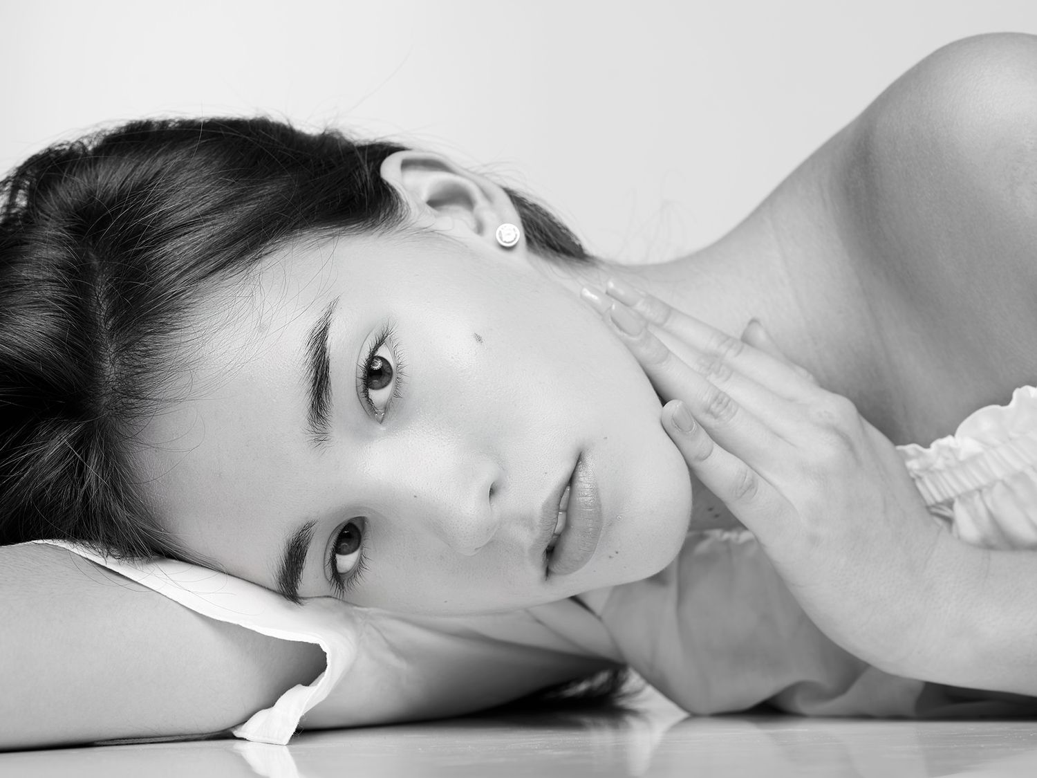 Black and white portrait of a young woman resting her head on her hands, gazing thoughtfully at the camera.