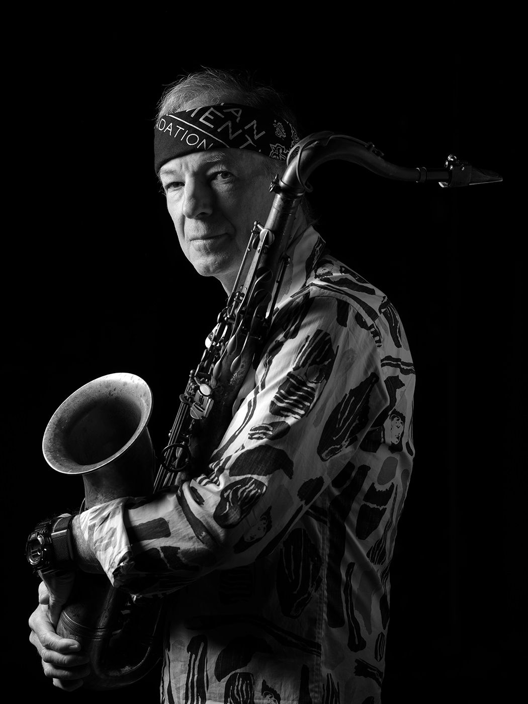 Black and white portrait of a male musician holding a saxophone, wearing a patterned shirt and headband. Bill Evans
