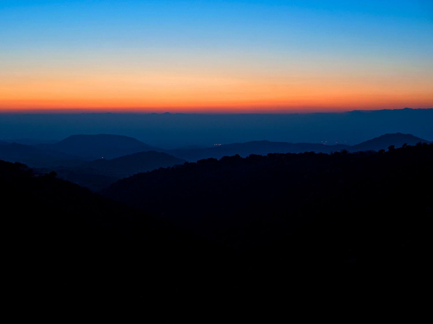 Stunning sunset silhouette over layered mountain ridges with vibrant orange and blue gradient sky at dusk.