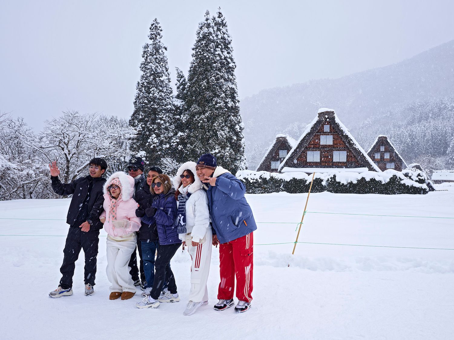 Group of friends posing together in snowy Shirakawa-go village Japan with traditional gassho-zukuri farmhouses in background.