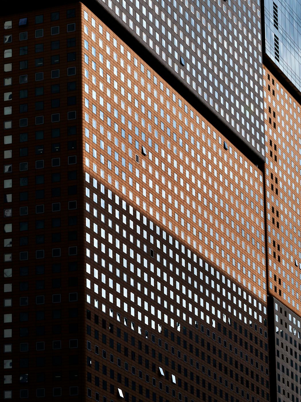 Close-up of a modern urban skyscraper facade featuring a grid pattern of small square windows on brown brick.